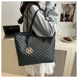 Detail of grey M-pattern tote bag with gold logo pendant in a professional office setting