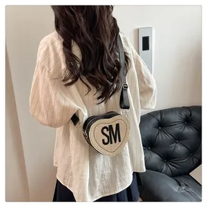 Detail of heart-shaped woven crossbody bag with black trim and SM letter logo
