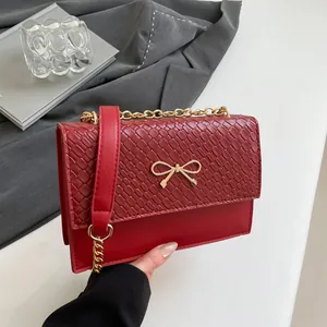Red woven flap handbag with golden bow decoration and metal chain shoulder strap