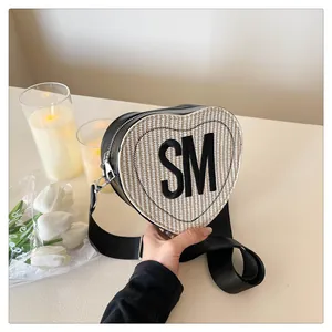 Detail view of heart-shaped woven crossbody bag with black SM letter embroidery