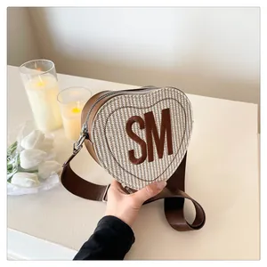 Detailed view of heart-shaped woven crossbody bag with brown trim and SM letter patch