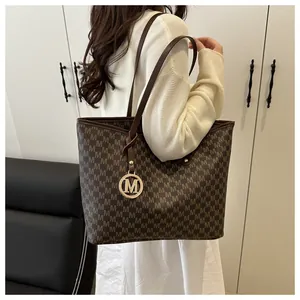 Side view of large brown tote bag with M-pattern print and gold metal charm pendant