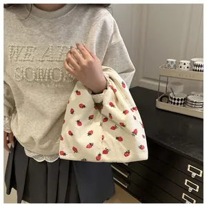 Détail du sac cabas en velours côtelé à motif fraise tenu par un mannequin en intérieur