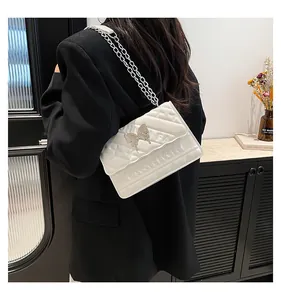 Detail of white quilted crossbody bag with silver butterfly clasp and chain strap