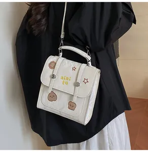 Detail van beige vierkante crossbodytas met cartoon borduurwerk en handgreep boven