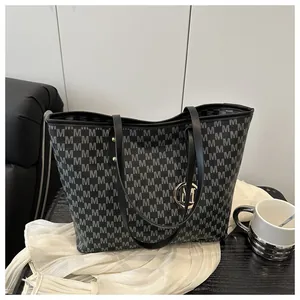 Detail view of large tote bag with grey M monogram pattern and black leather handles