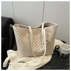 Detail of a beige tote bag featuring M-letter print and a gold-tone metallic logo charm