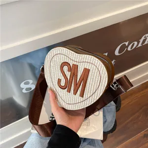 Heart-shaped crossbody bag featuring cream woven texture and brown leather accents