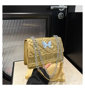 Detail of gold quilted crossbody bag featuring a white butterfly and silver chain strap