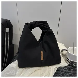 Détail du sac cabas en toile noire montrant la poignée nouée et l'étiquette logo en cuir