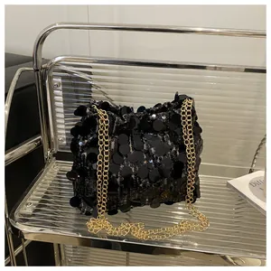 Detail of black sequin shoulder bag with golden chain strap on a modern display