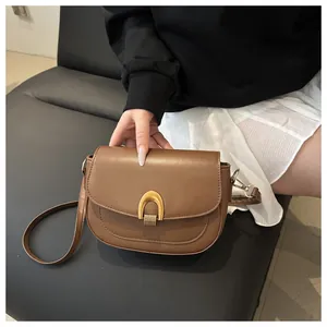 Gros plan sur la texture du cuir fin et la boucle en métal doré du sac besace marron