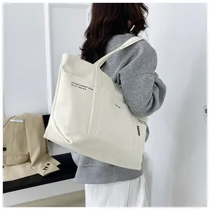 Macro view of creamy white canvas tote bag showing side pocket and red brand label