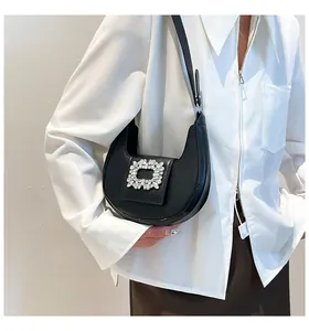 Model wearing a black crescent shoulder bag with a large rhinestone square buckle detail