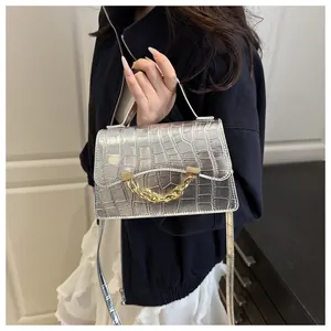 Detail of silver crocodile embossed handbag featuring a bold gold chain handle accent