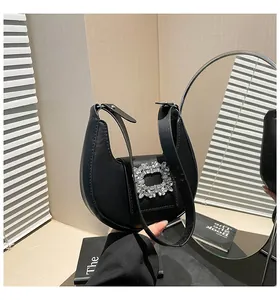 Detail of a black crescent handbag with a sparkling square crystal buckle in soft light