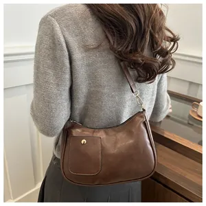 Detailed view of dark brown PU crescent shoulder bag with golden buckle on a grey sweater