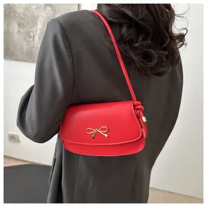 Detail of red faux leather shoulder bag with a stylish gold bow metal buckle clasp