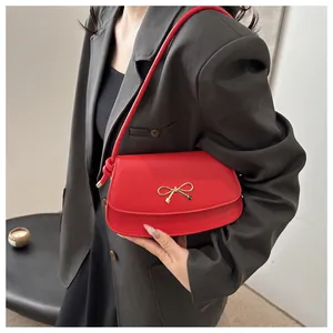 Close-up of red leather underarm bag featuring a gold bow buckle on a grey suit jacket