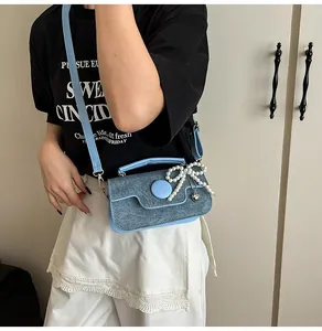 Detail of light blue denim crossbody bag featuring pearl bow and silver heart charm