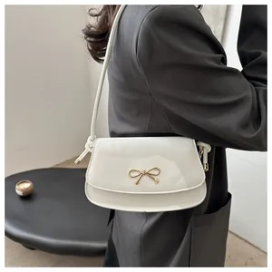 Detail of cream underarm bag with gold bow clasp and sleek patent leather finish