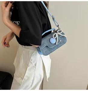 Detail of light blue denim texture bag featuring a large pearl bow ornament on the flap