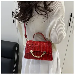 Detail of red crocodile texture small box bag with gold chain strap on a model