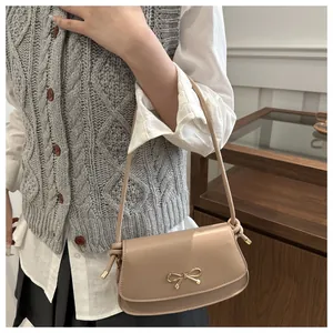 Detail of light beige underarm bag featuring a golden bow metal buckle and flap design