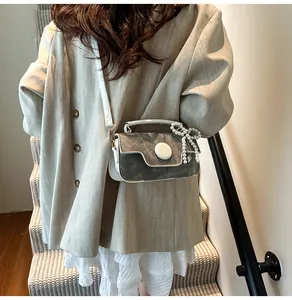 Detail view of contrast color crossbody bag featuring white piping and pearl bow charm