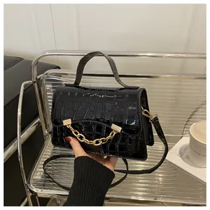 Close-up of black glossy croc-embossed leather handbag with gold chunky chain detail