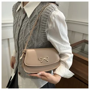Detail of a chic cream shoulder bag with a gold bow buckle worn on the shoulder