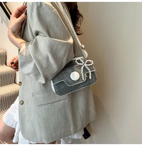 Detail of grey crossbody bag with elegant pearl bow and white trim decoration