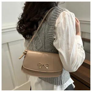 Detail of beige shoulder bag featuring a golden bow buckle and knotted strap detail