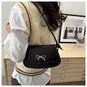 Close-up of a black leather underarm bag featuring a golden metal bow and a knotted strap detail