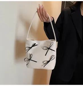 Détail du sac fourre-tout crème avec nœuds noirs porté à l'épaule pour femme