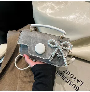 Detail of grey denim crossbody bag featuring pearl bow charm and silver heart pendant