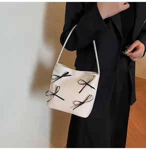 Détail du sac seau beige minimaliste avec nœuds noirs décoratifs et bandoulière fine