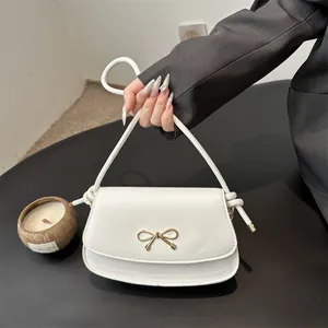 Chic white leather underarm bag with gold bow ornament and knot handle for women