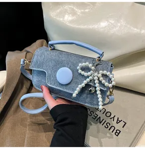 Detail of blue denim handbag with pearl bow charm and leather handle held by model