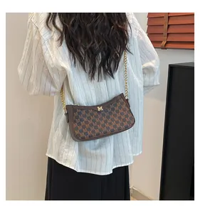 Close-up of brown monogram crossbody bag with gold chain strap worn by a model