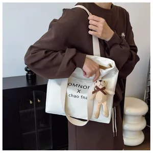Close-up of stylish white tote bag with black lettering and a cute teddy bear charm