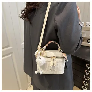 Detail of white textured crossbody bag with silk scarf handle and plush fur ball charm