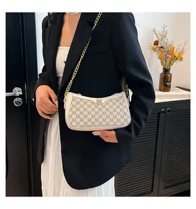 Detail of a chic cream shoulder bag with M-pattern print and gold chain strap on a model