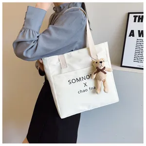 White canvas tote bag with black letter print and cute brown bear pendant on a model
