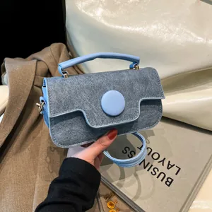 Blue denim texture handbag with circular buckle and top handle in a lifestyle setting