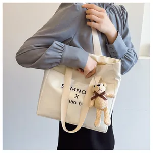 Detail of a beige tote bag with black lettering and a cute brown knitted bear charm