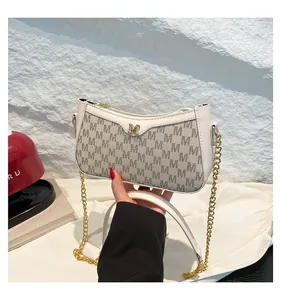 Detail of cream crossbody bag with gold chain and embossed letter pattern