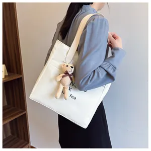 Close-up of a white leather tote with woven strap and a cute beige teddy bear pendant