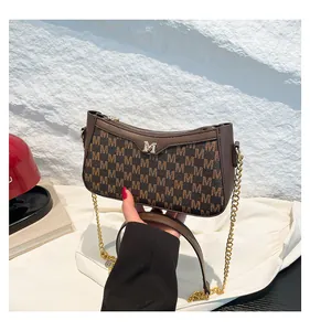 Detail of a brown leather shoulder bag featuring M letter patterns and gold logo accents