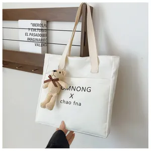 Detail of white nylon tote bag with black letter print and cute brown bear pendant charm